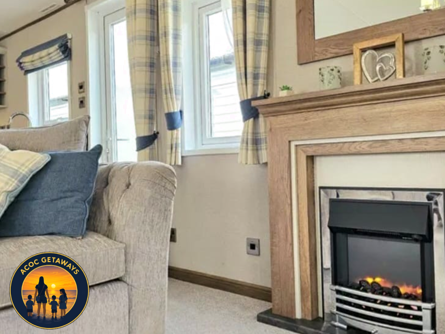 Living room corner with a beige tufted sofa with pillows, a fireplace with wood trim, and windows with plaid curtains tied back, letting in natural light.