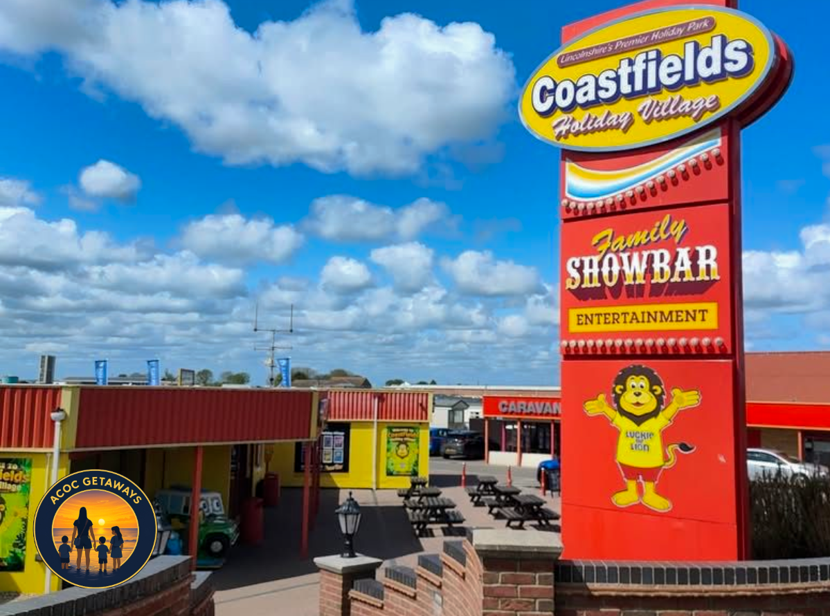 Sign for Coastfields Holiday Village featuring a lion mascot named Lucky Lion, with blue sky and clouds in the background.