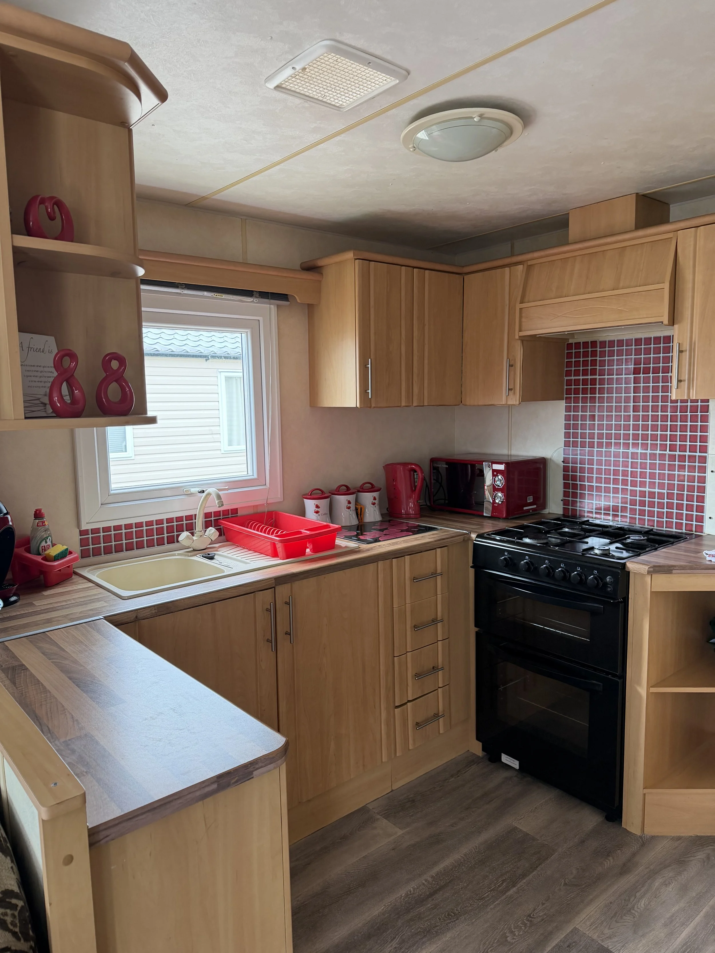 A kitchen with wooden cabinets, red kitchen appliances, a window, a sink, and a stove.