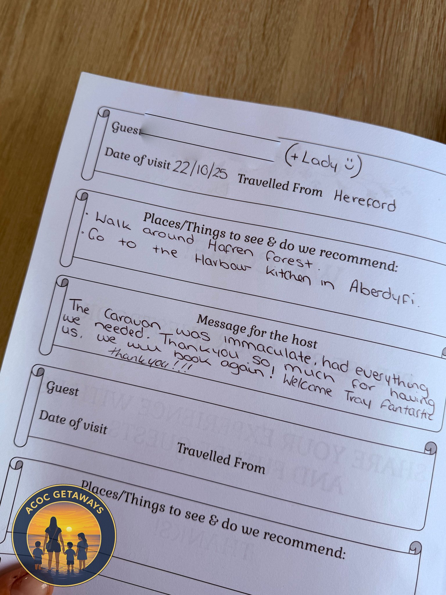 A handwritten guestbook page with notes about a visit to Hereford, including places to see like Haren Forest and the Aberdyfi Kitchen, and a thank you message to the host. There is a small logo in the lower left corner with a silhouette of a family h