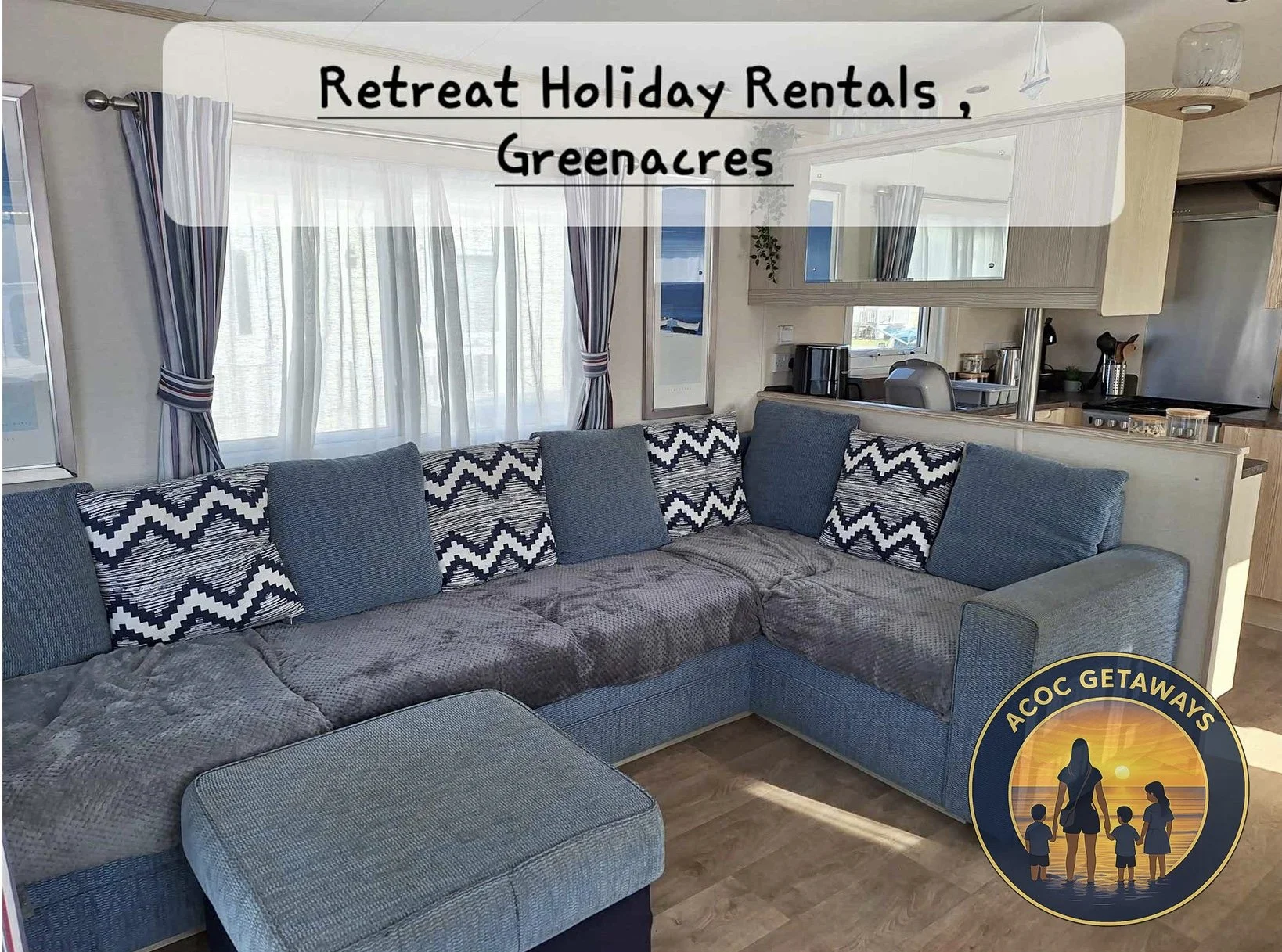 A cozy living room with a large sectional sofa adorned with patterned and solid blue cushions. Behind the sofa, large windows with striped and sheer curtains allow natural light into the room. The opening into the kitchen shows a coffee machine, kettle, and other kitchen appliances. There is a logo in the bottom right corner with a picture of a woman and children at sunset, with the text "ACOC GETAWAYS".