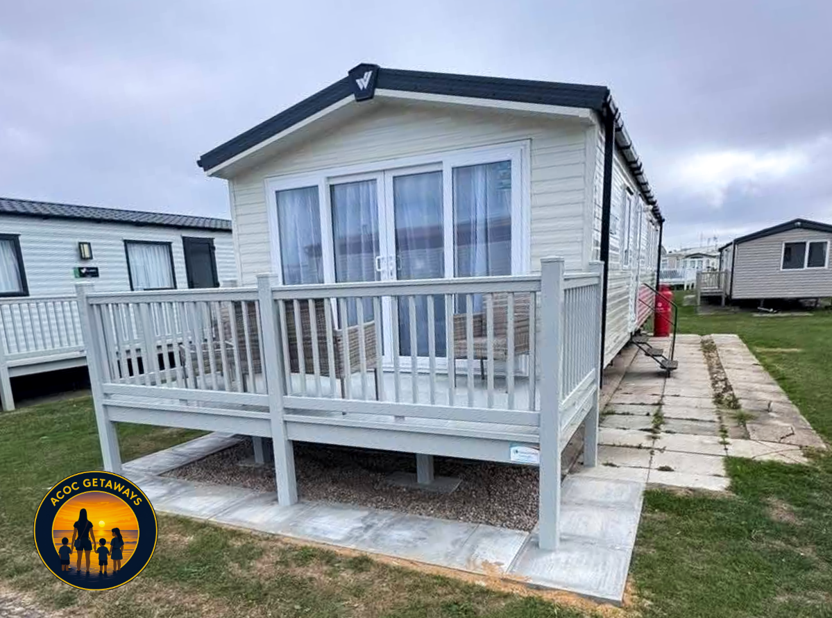 A white mobile home with a front porch and sliding glass doors, located in a park with similar homes and green grass.