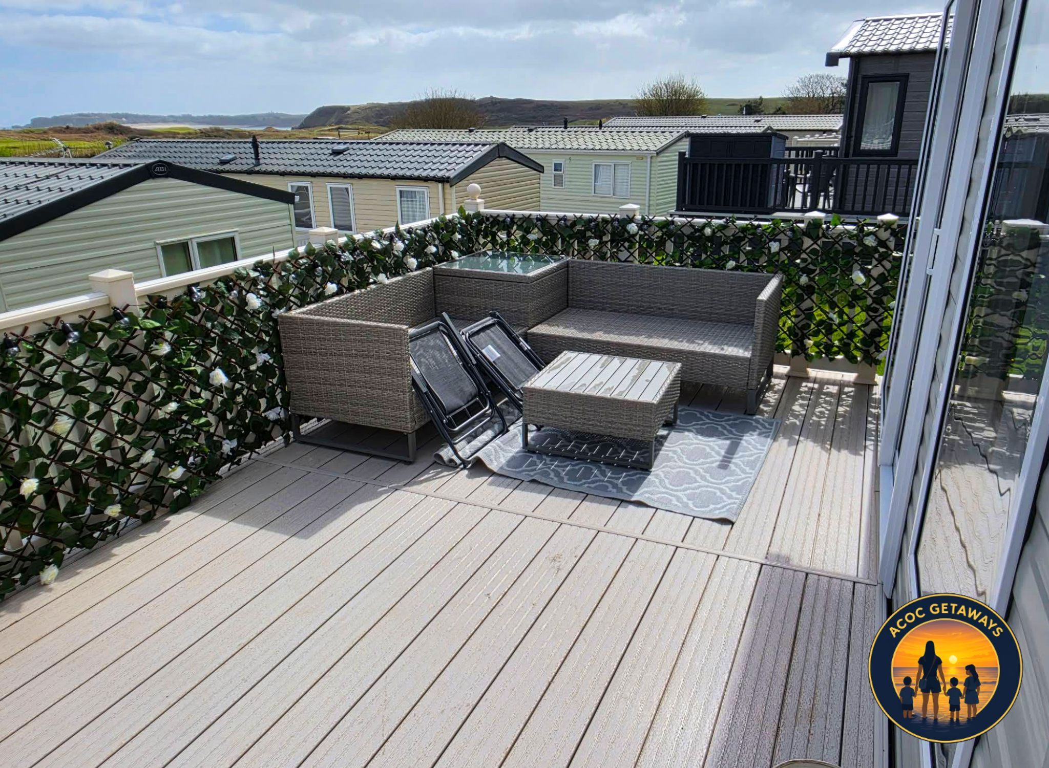 Balcony overlooking neighboring houses with tiled roofs, surrounded by greenery and distant hills under a cloudy sky.