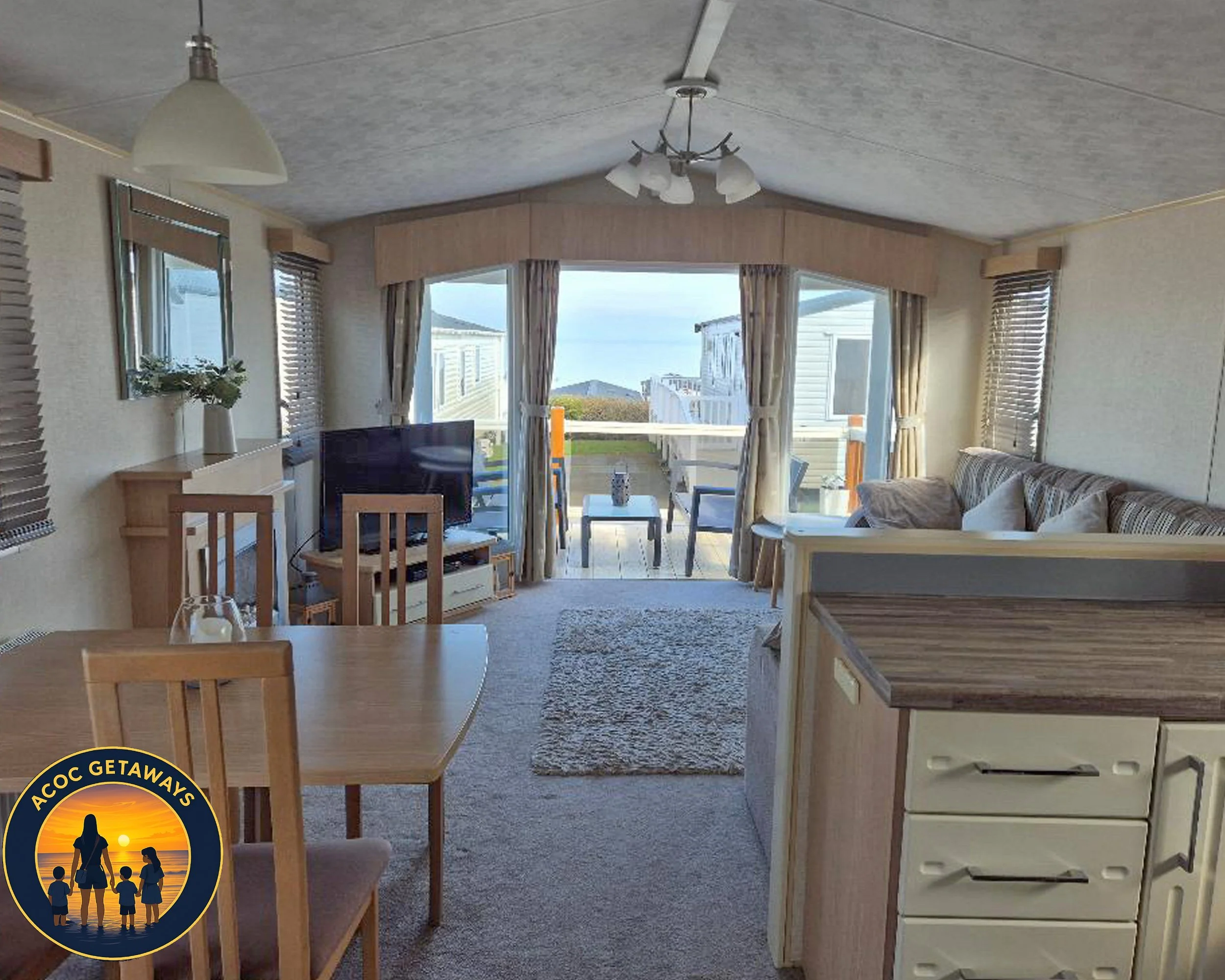 Living room with a sofa, a TV on a stand, a dining table with chairs, and sliding glass doors opening to a balcony with outdoor furniture and a view of the ocean.