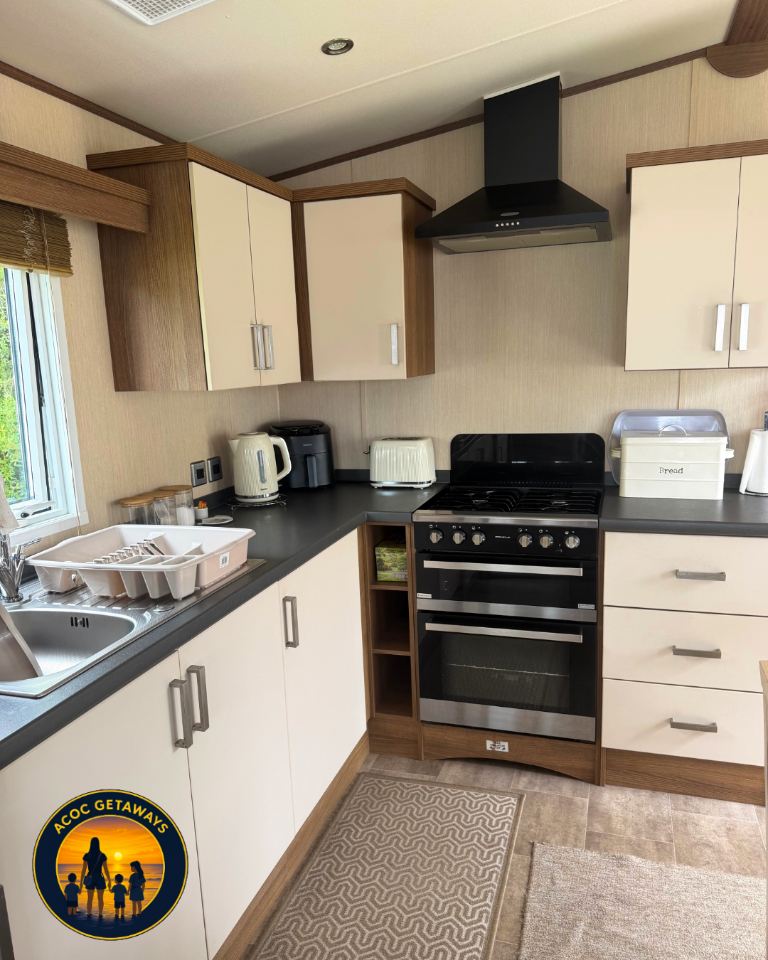 Kitchen with white cabinets, black countertops, stove, range hood, and small appliances including kettle, toaster, and coffee maker, in a cozy setting.