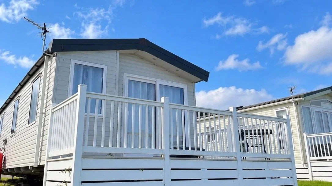 White house with large windows, a porch railing, and a blue sky with scattered clouds.