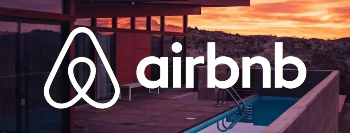 Modern house with a wooden deck, swimming pool, and mountain sunset view, with Airbnb logo overlay.