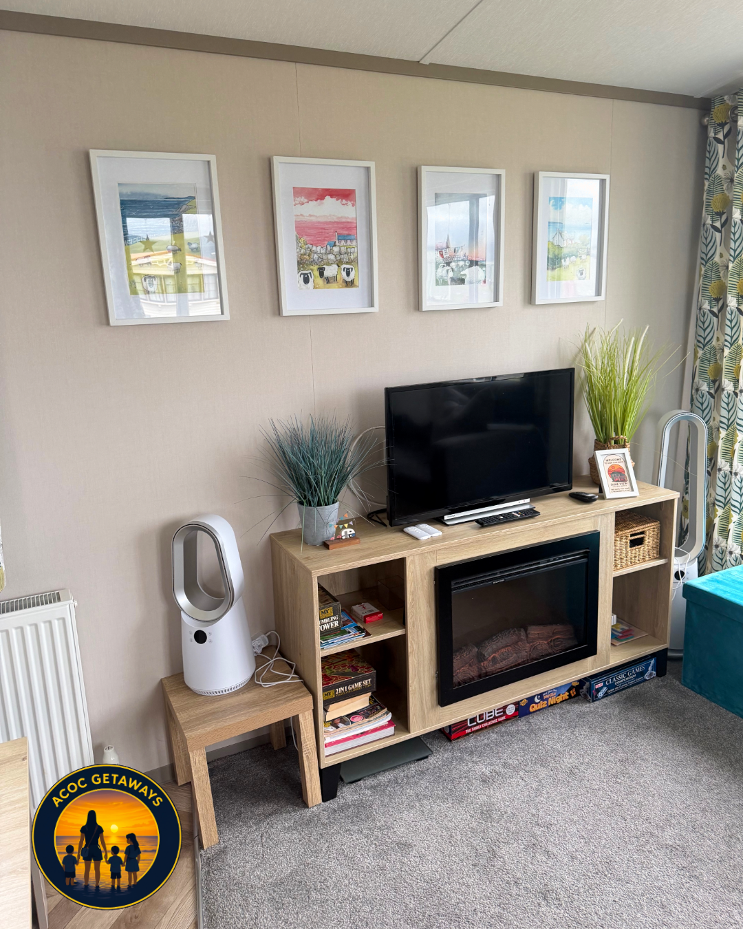 Living room with a wooden TV stand, flat-screen TV, decorative plants, framed artwork on the wall, a Dyson fan, and curtains with a green and yellow leaf pattern.