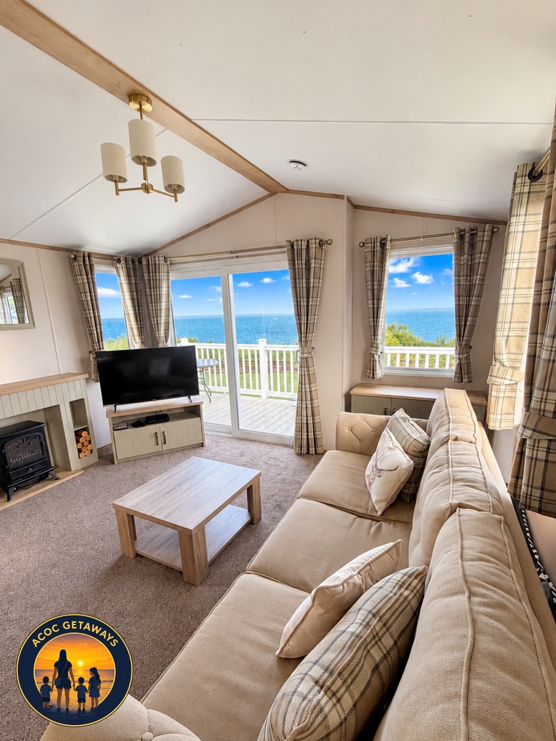 Coastal living room with beige sofa, plaid curtains, wood coffee table, flat-screen TV, fireplace, and large windows showing ocean view