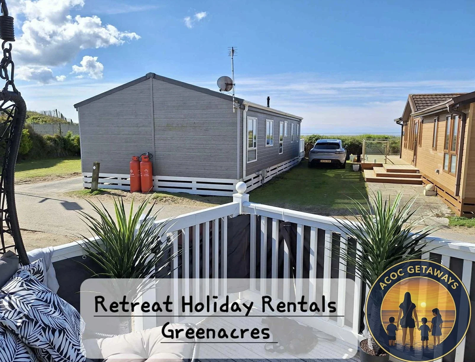 View from a balcony overlooking a grassy area with two mobile homes, a car, and a clear blue sky in Greenacres. The balcony has potted plants and outdoor furniture with a logo for ACoc Getaways.