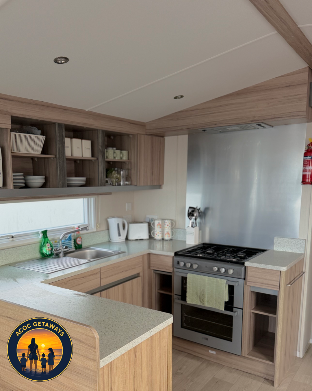 Kitchen with wooden cabinets, stainless steel stove, white kettle, toaster, mugs, and a window above the sink.