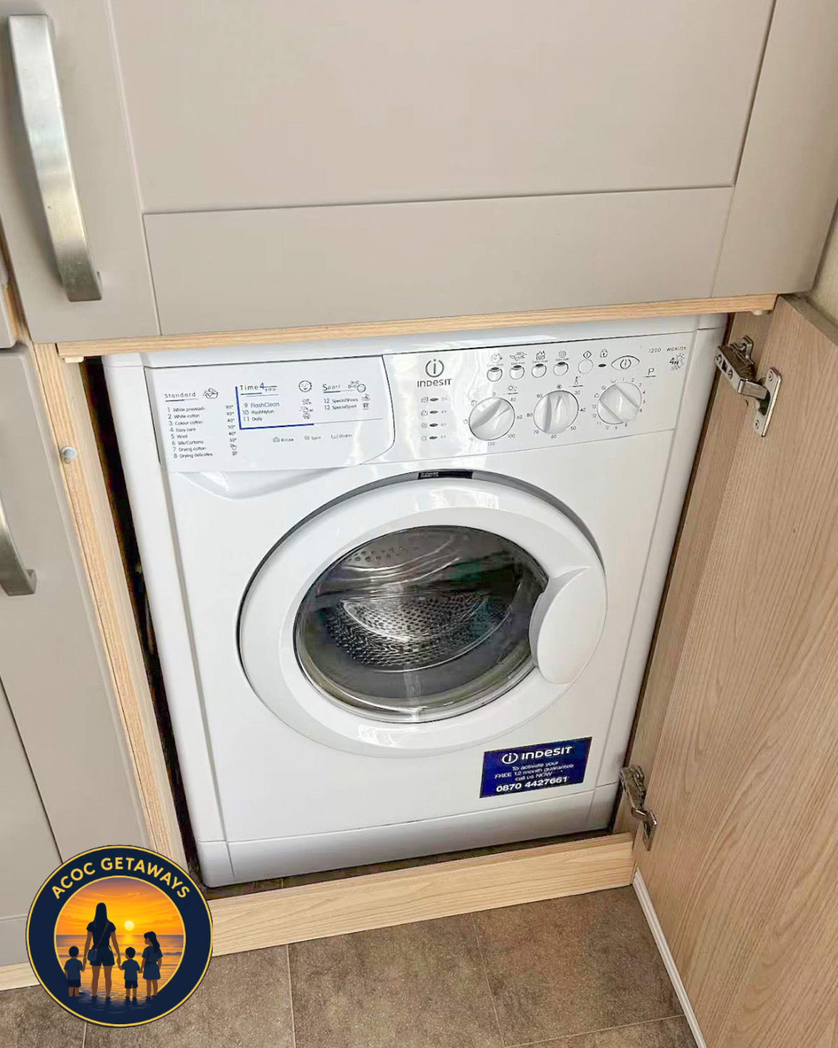 A front-loading washing machine placed under a light wood cabinet with a stainless steel handle, in a laundry room with tiled floor, advertising a promotion at the bottom left corner with a silhouette of a family at sunset and the text 'A COC GETAWAY