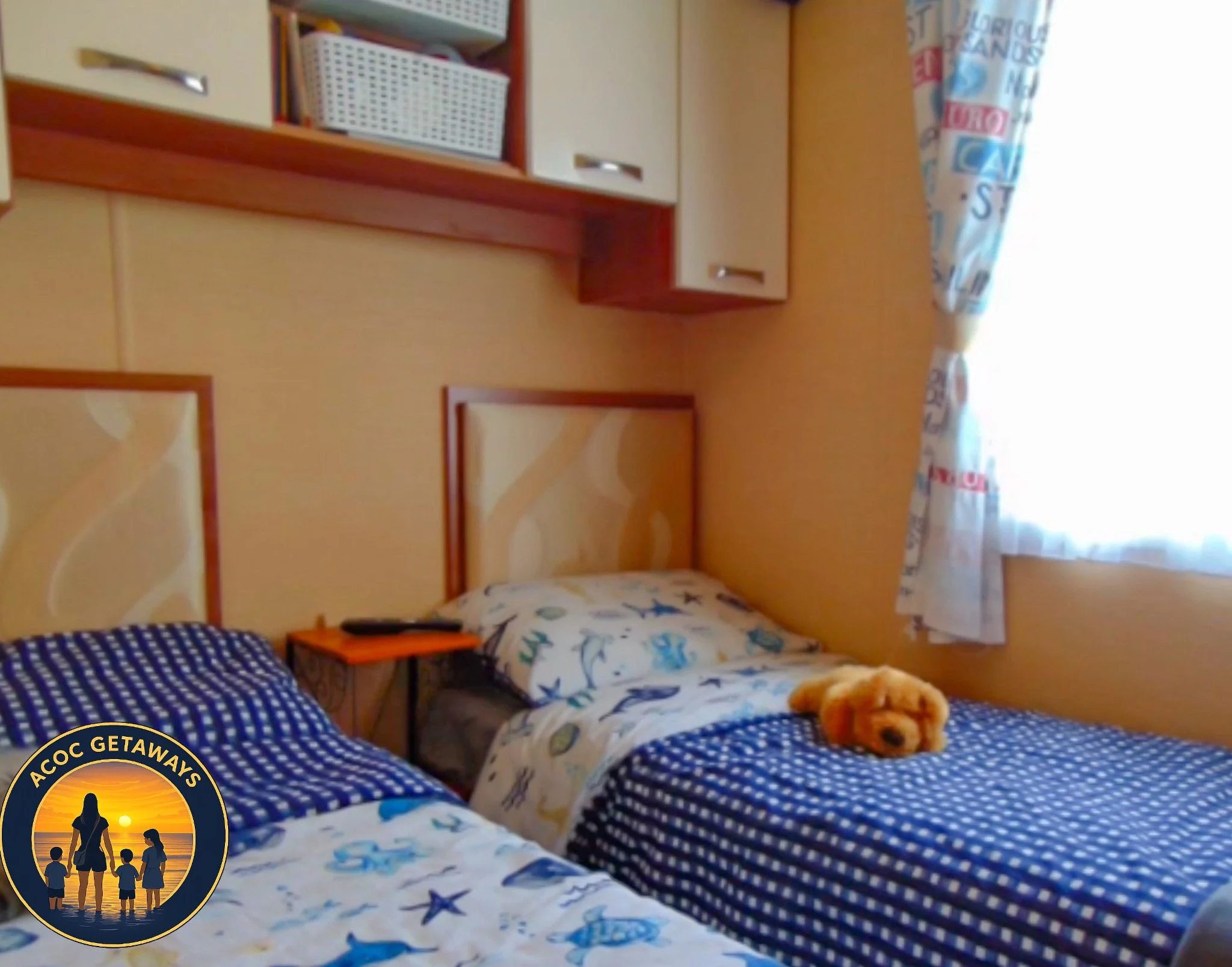 A cozy bedroom with two twin beds decorated with seahorse and starfish patterned bedding. There is a small stuffed animal on one bed, a bedside table with a remote control, and a window with marine-themed curtains allowing sunlight into the room.