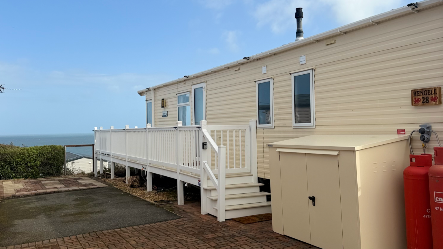 Beach house with a white porch, ocean view, and propane tanks on the side.