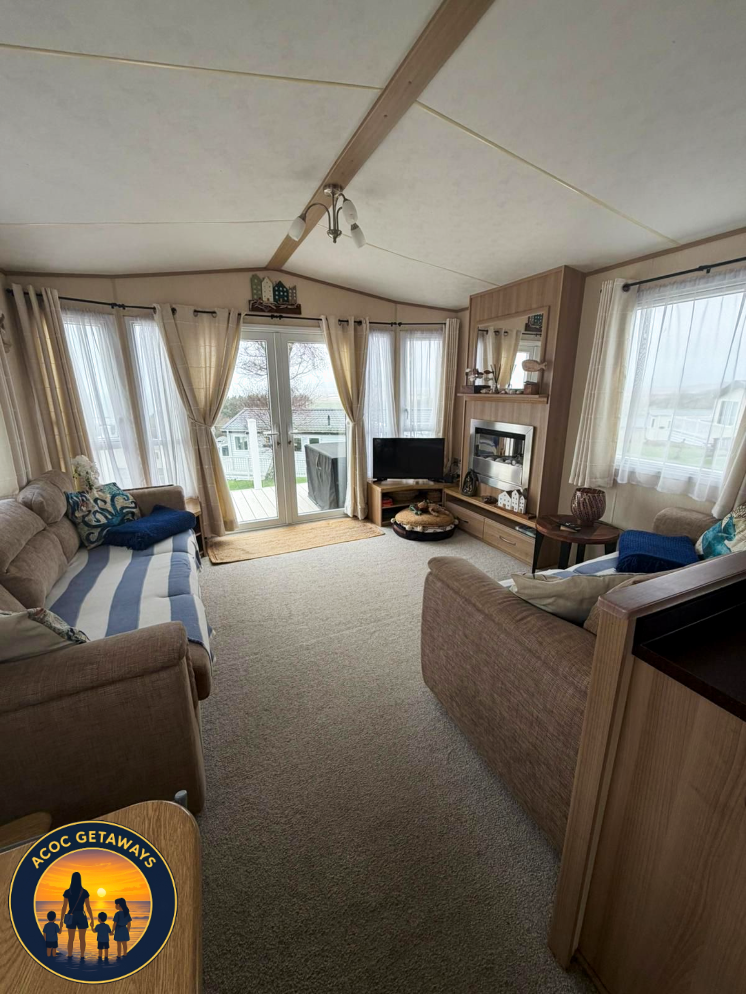 Living room with beige sofas, large windows with curtains, a small television, and a door leading outside.