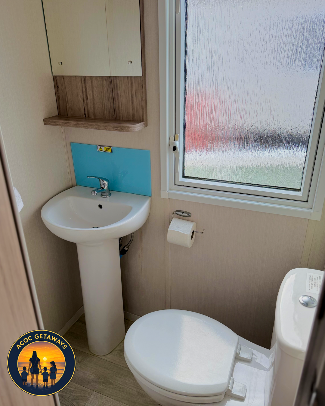 Small bathroom with a pedestal sink with a blue backsplash, a window with frosted glass, a toilet, a toilet paper holder, and a small cabinet above the sink.