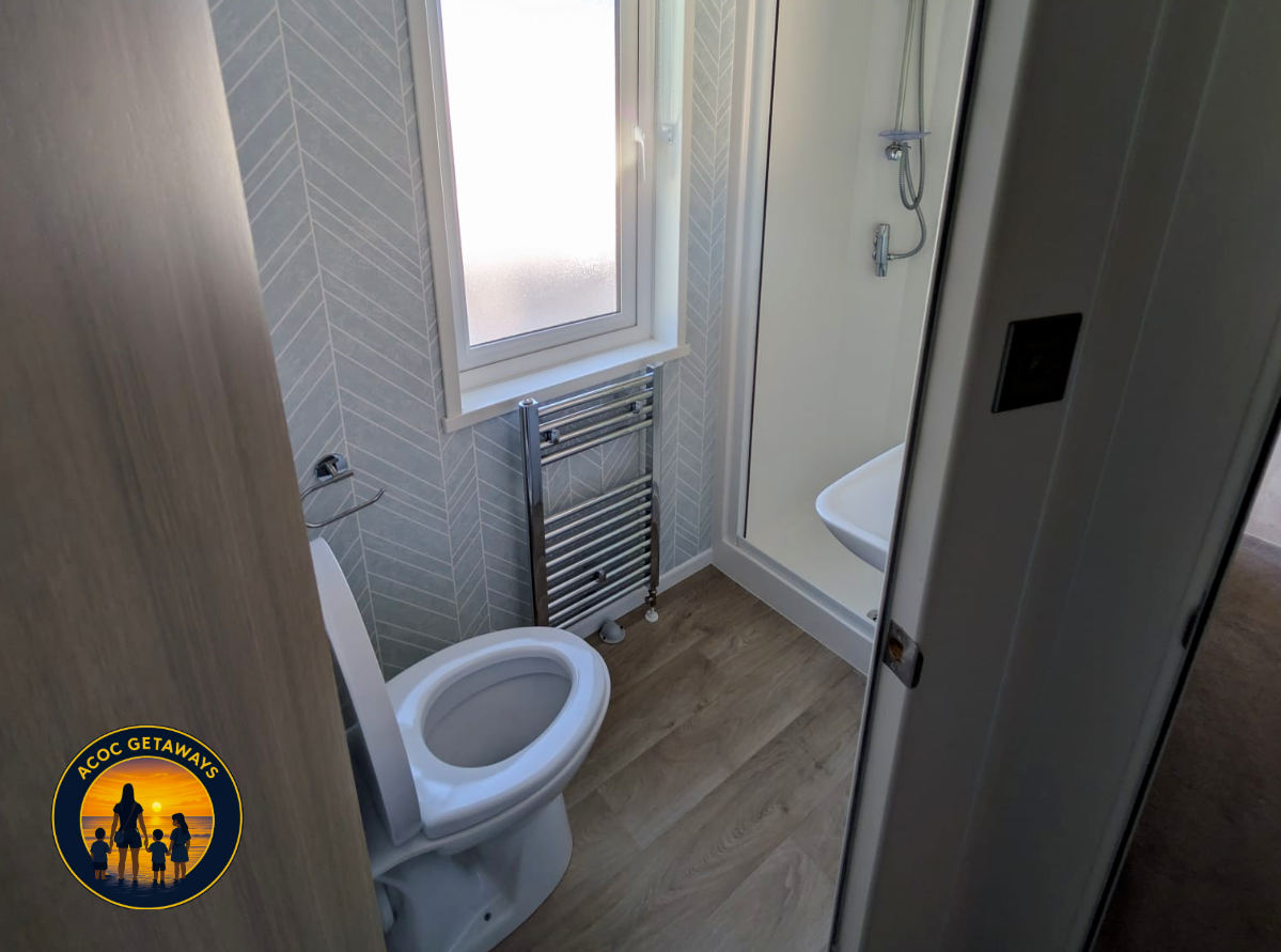 Compact bathroom with a toilet, frosted window, wall-mounted towel warmer, and a shower stall with a glass door and handheld shower head.