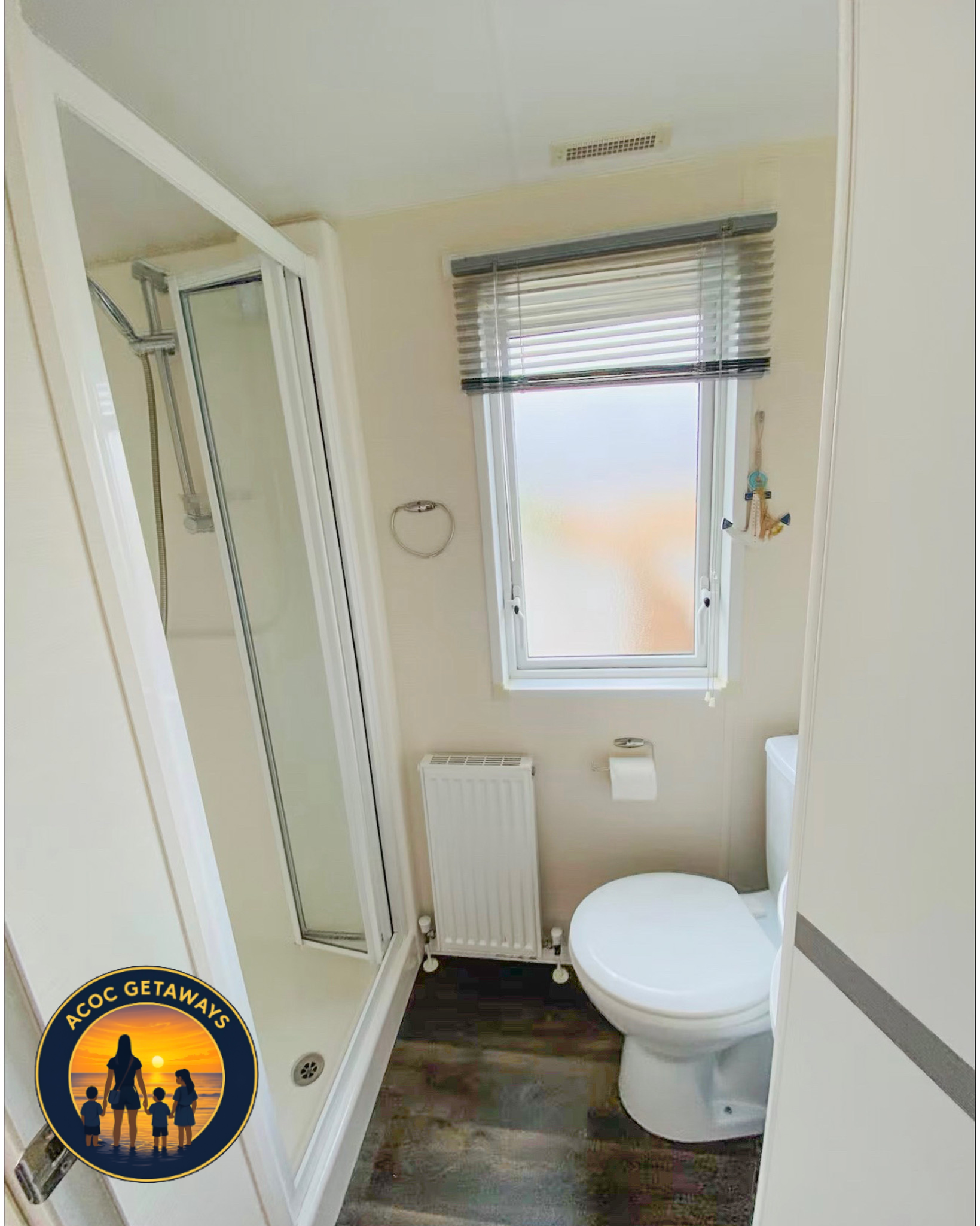 Small bathroom with a shower stall on the left, a window with blinds on the back wall, a white radiator below the window, a toilet on the right, and a small trash can in the corner near the toilet.