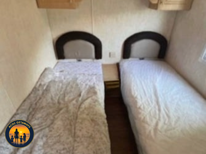 Two single beds with brown headboards separated by a small wooden nightstand in a small room.