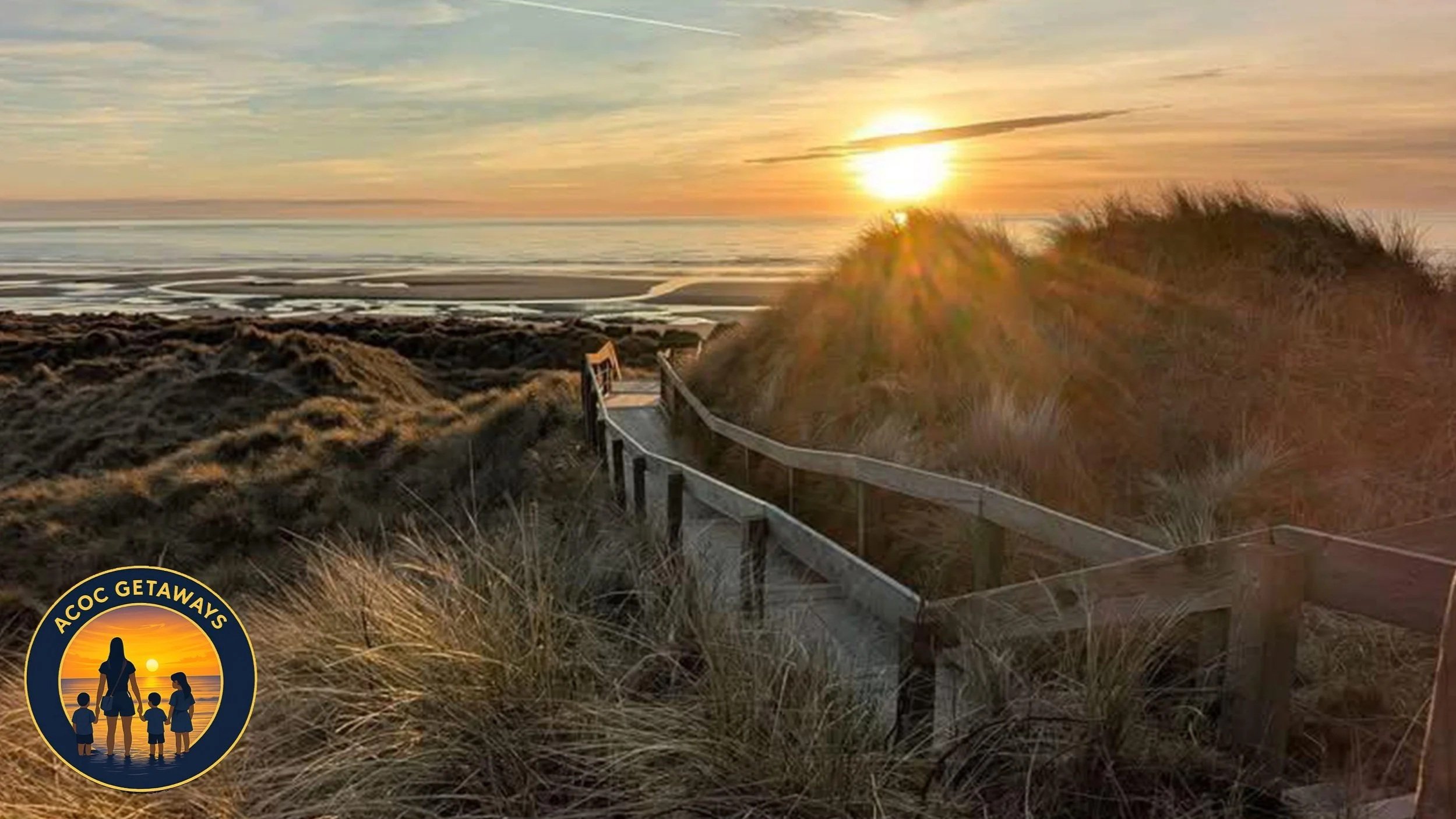 A wooden pathway leading to a beach at sunset, with grassy dunes on either side and the sun setting over the ocean in the background.