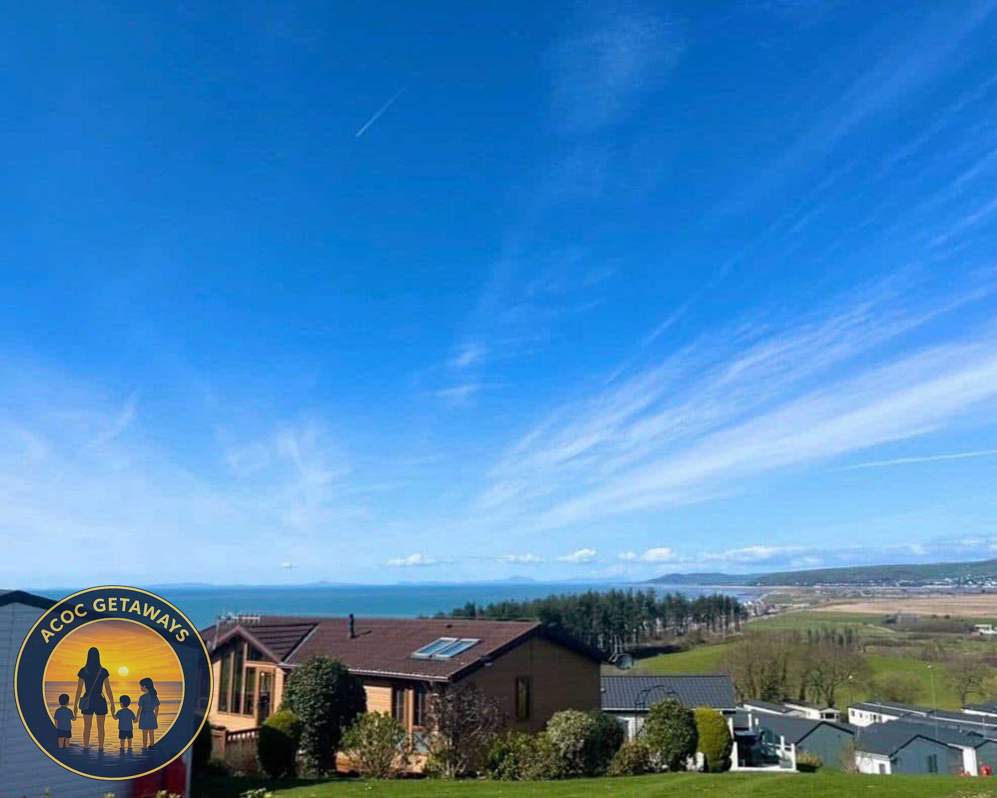 A scenic view of houses with a coastline and ocean in the background under a blue sky with wispy clouds.