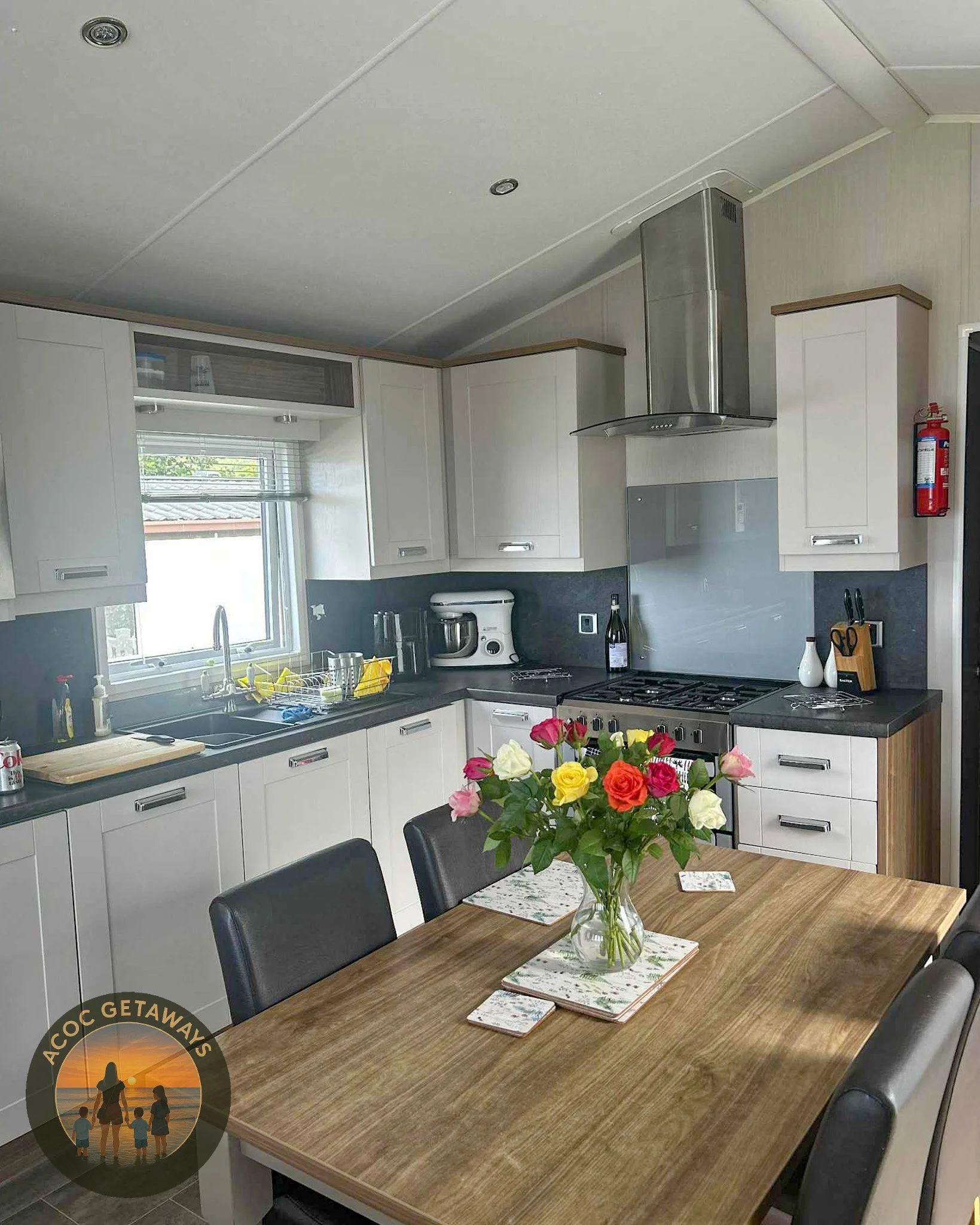 Kitchen with white cabinets, a black countertop, a stainless steel stove range, a vase of mixed roses on a wooden dining table, and a window behind the sink.