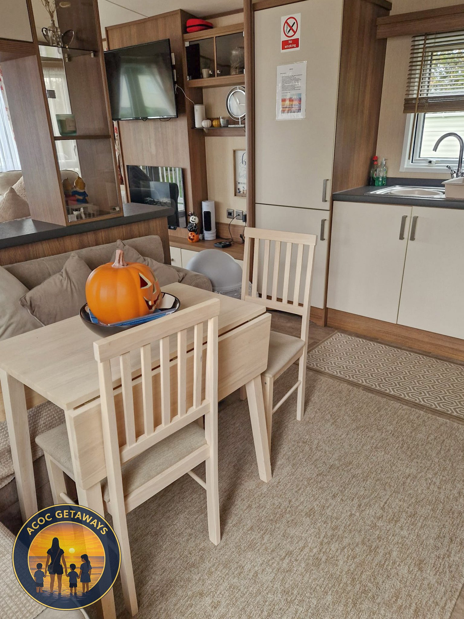 Living room and kitchen area with a dining table, chairs, and a Halloween pumpkin decoration on the table.