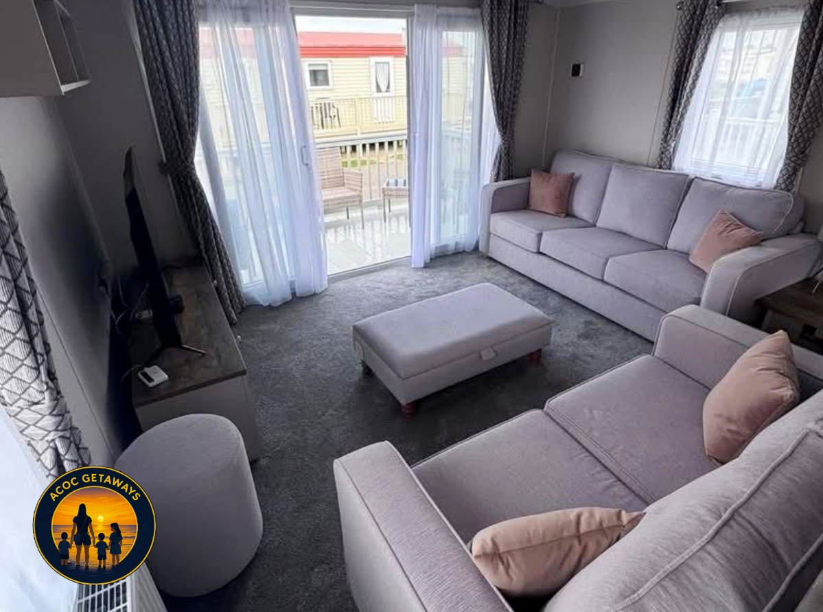 Living room with light-colored sofas, pink cushions, a television, a sliding glass door leading to a balcony, and curtains.