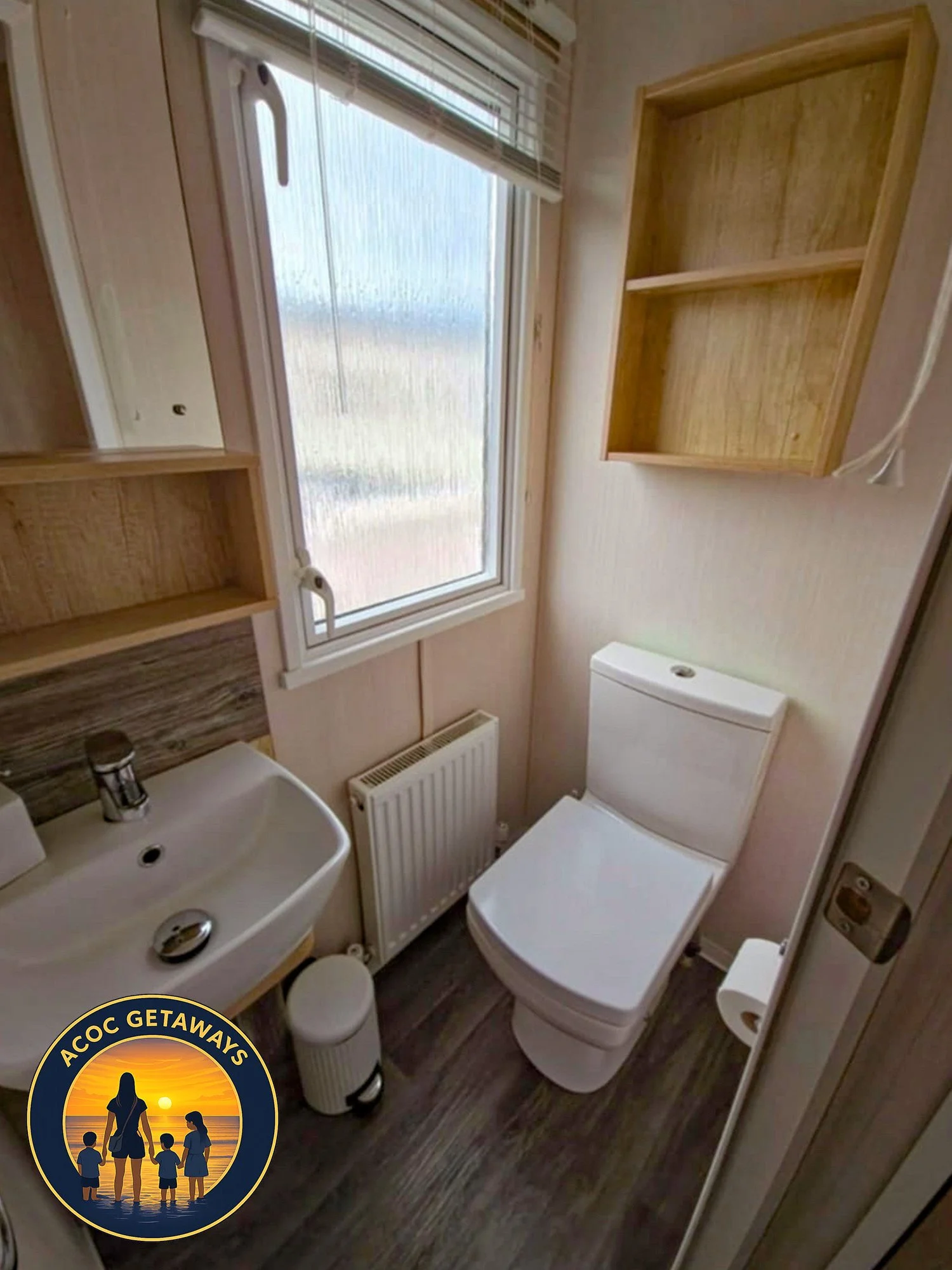 Small bathroom with a white toilet, a compact sink, a window with blinds, and wooden shelves on the walls.