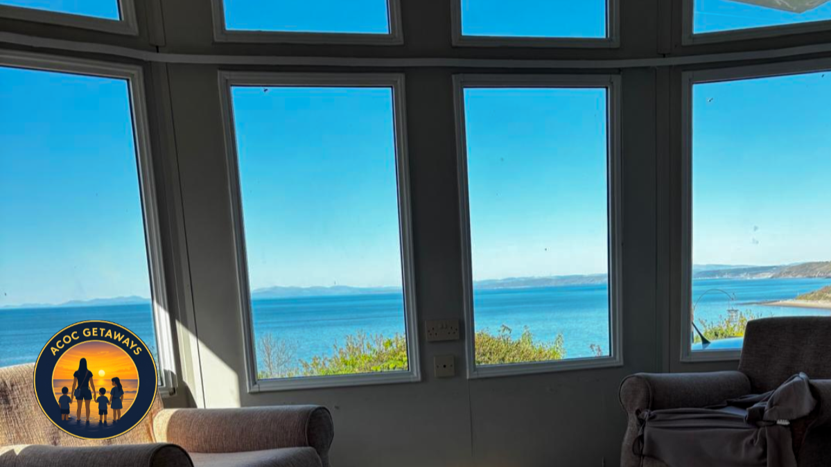 View of the ocean through large bay windows from inside a house with armchairs.