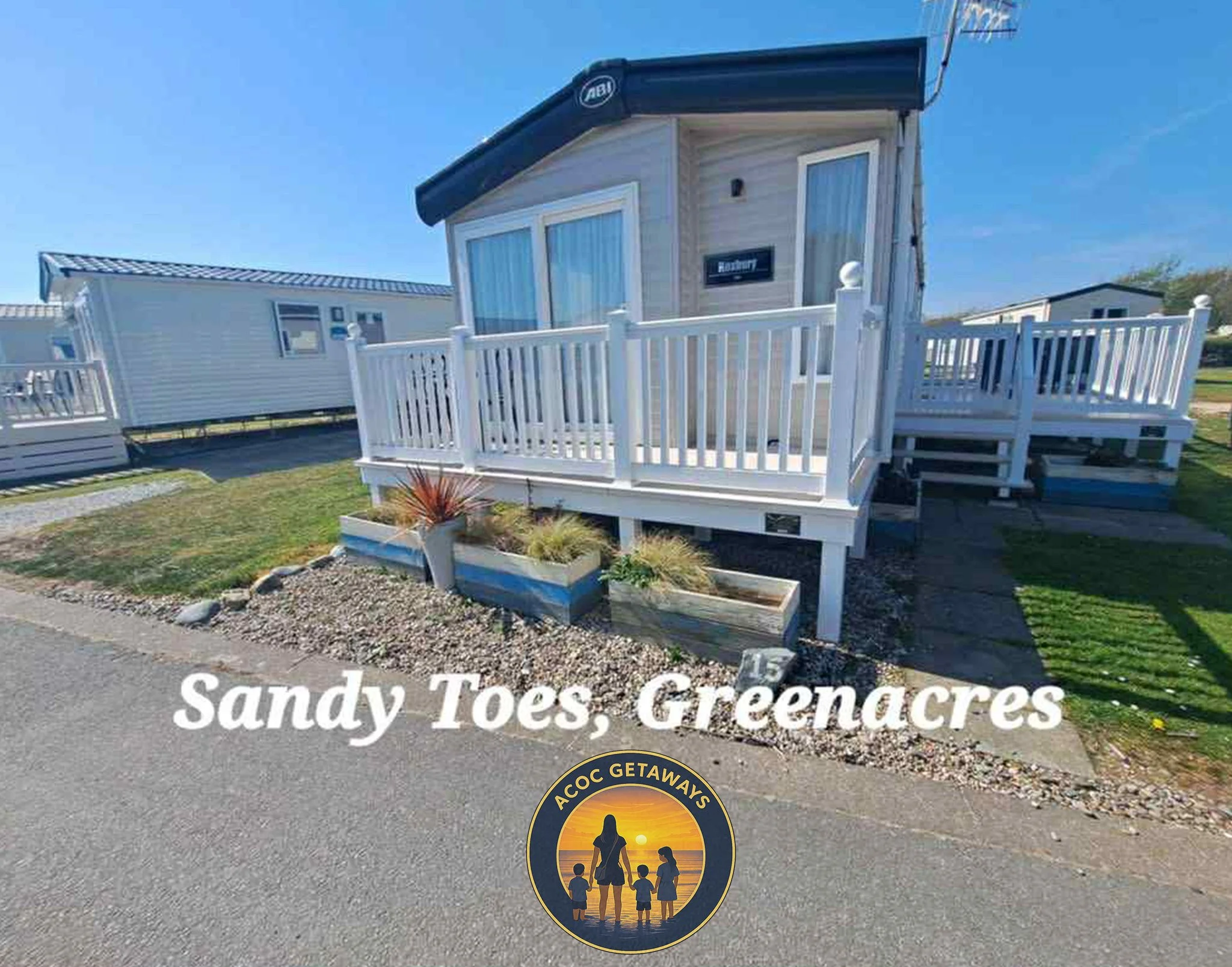 A small light-colored cabin with a white porch railings and steps, green grass, a small garden with plants, and a bright blue sky. Text overlay says 'Sandy Toes, Green Acres' with a circular logo of a woman and children by the beach.