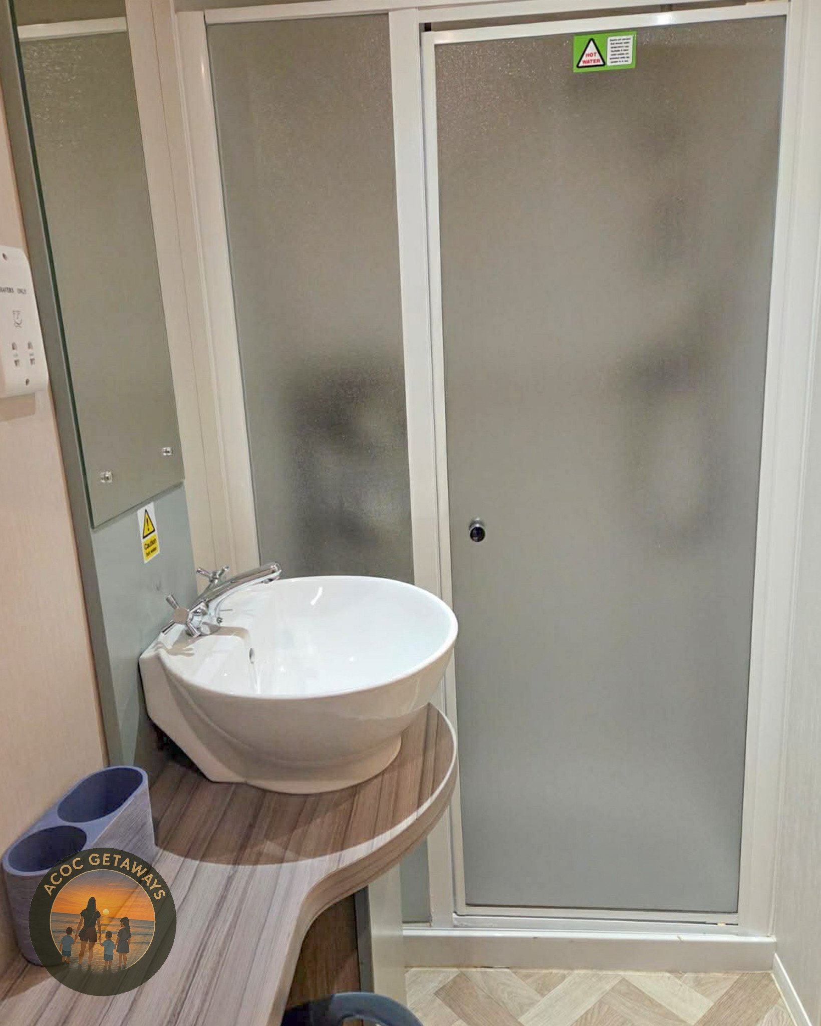 A small bathroom with a frosted glass shower door, a white sink with a wooden countertop, and a mirror on the wall.