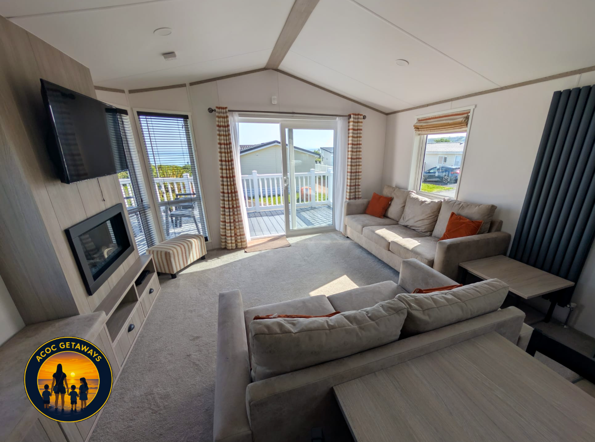 Living room with beige sofas, a wall-mounted TV, a fireplace, a sliding glass door leading to a balcony, and windows with striped curtains.