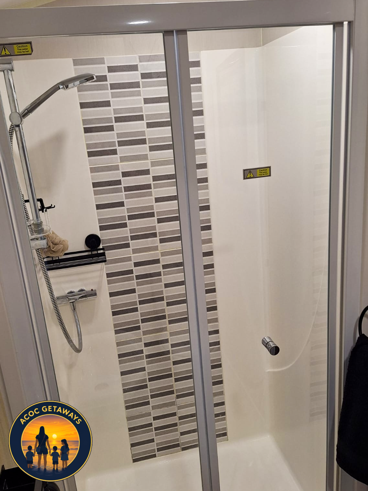 Inside a shower stall with a glass door, showerhead, and tiled wall with a horizontal striped mosaic pattern.