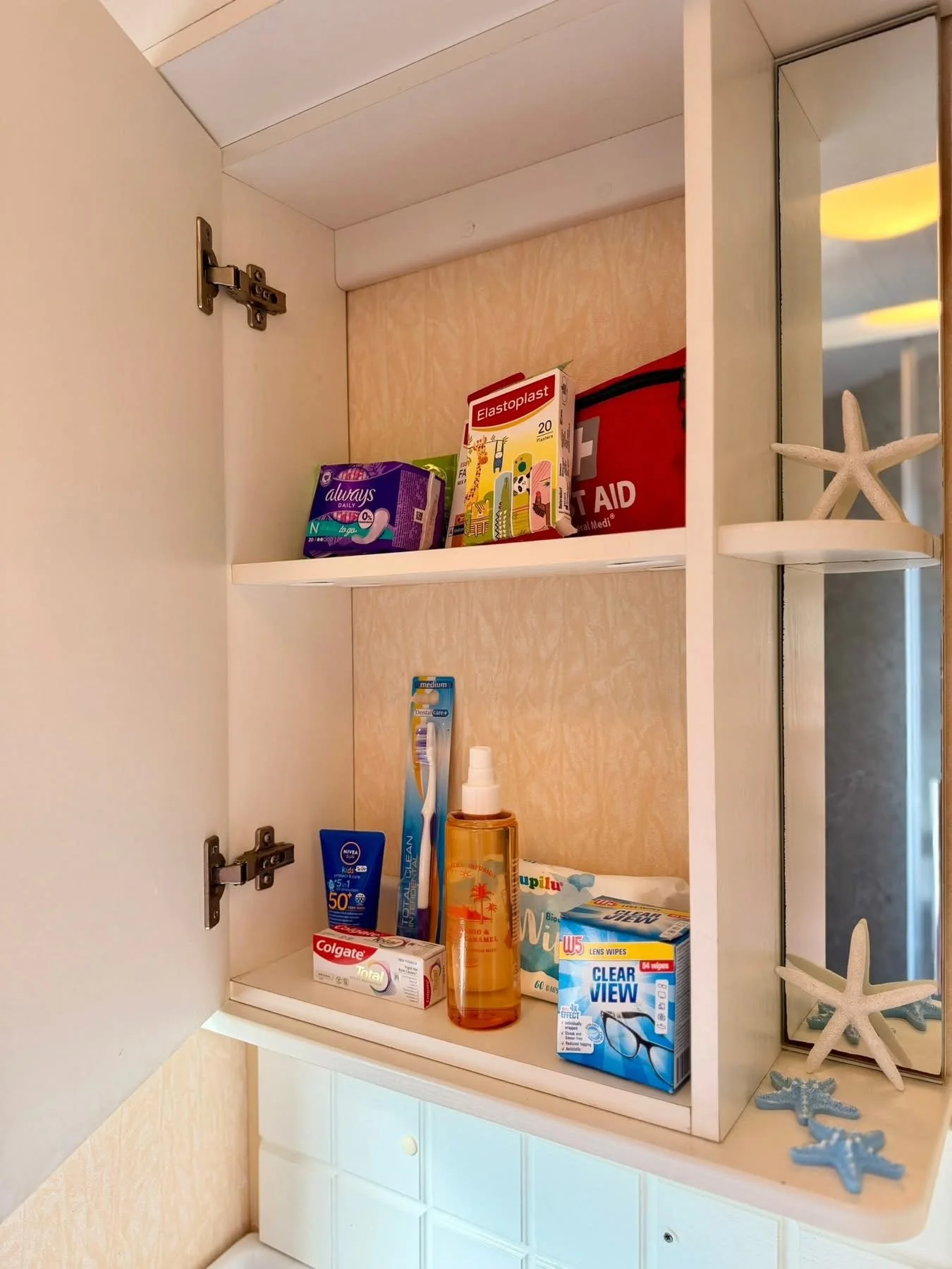 Open bathroom medicine cabinet with various personal care and health items including toothpaste, sunscreen, hand sanitizer, and medical supplies.
