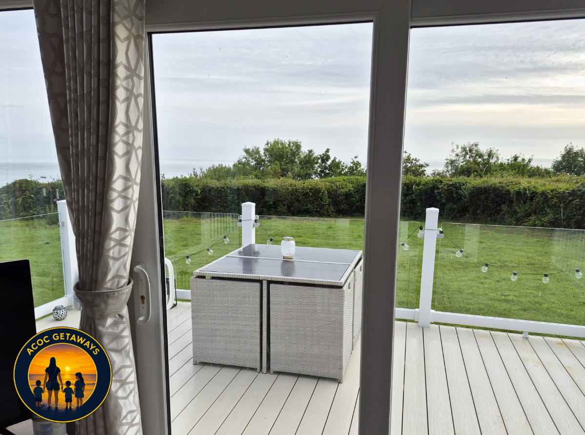 View of a backyard patio with grass, trees, and a cloudy sky, seen through glass sliding doors with patterned curtains on the side.