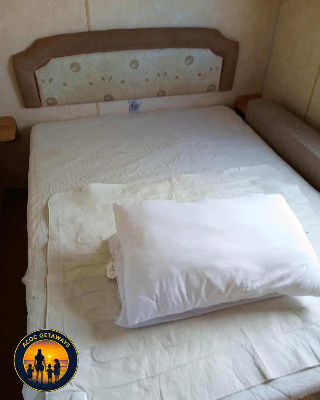 Unmade hotel bed with a pillow on top, a headboard, and side tables in a small room.
