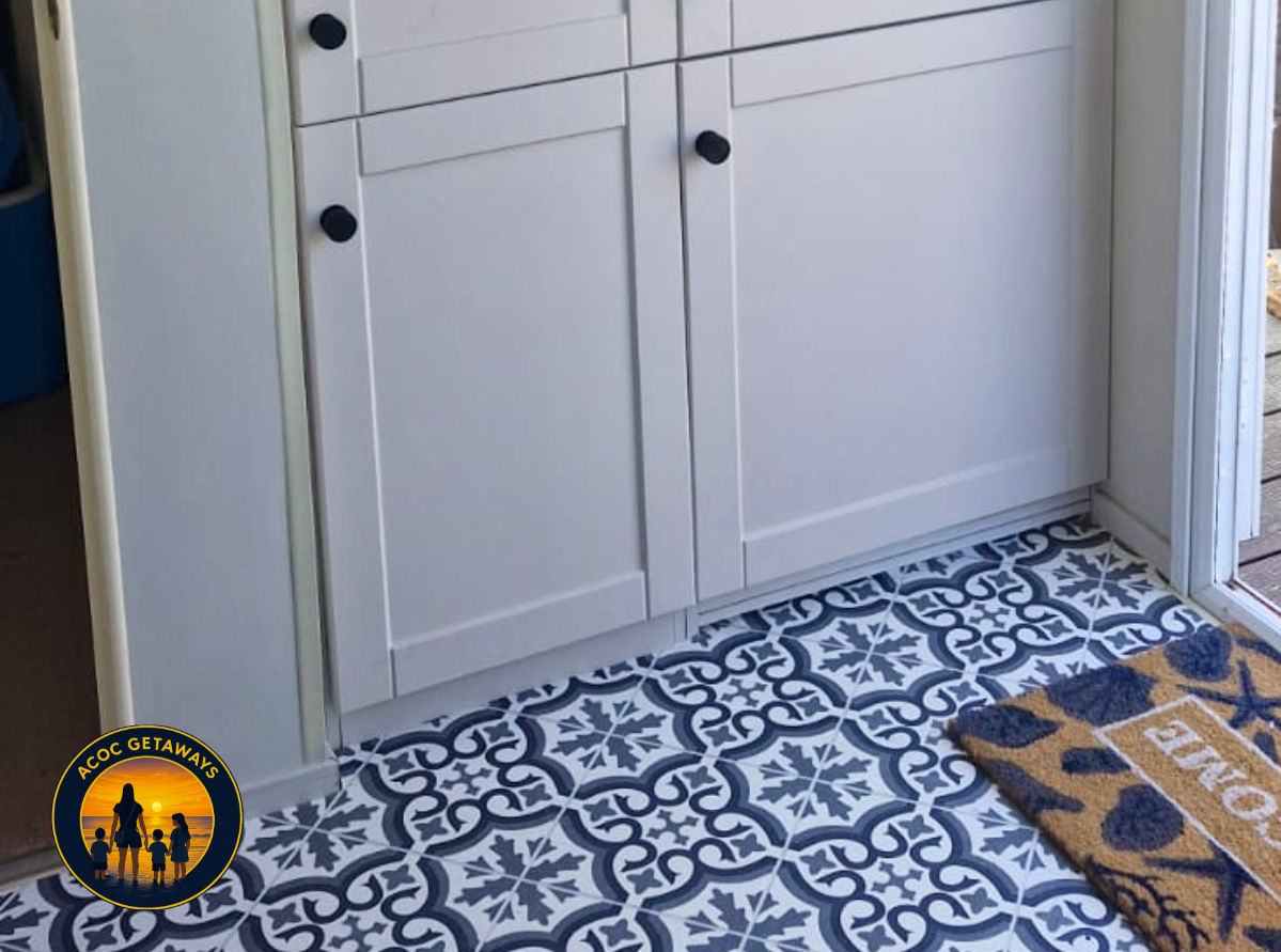 Close-up of a white cabinet with black knobs on a patterned tile floor, next to a wooden deck and a door threshold.