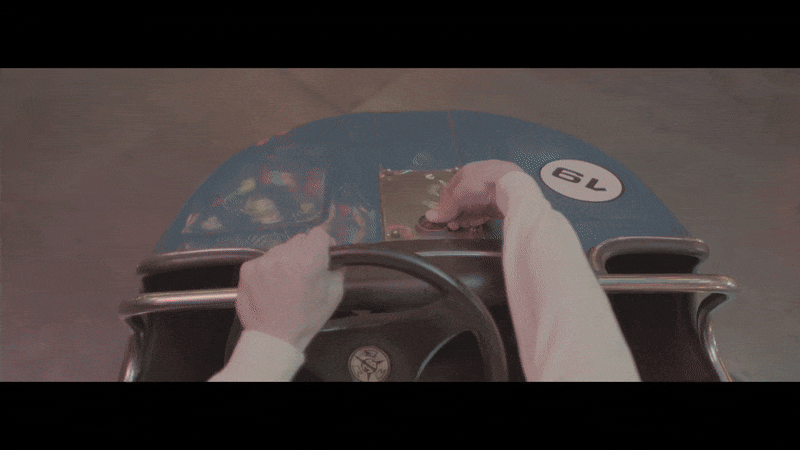 Nahaufnahme einer Hand, die einen Zehnerkarton im Inneren eines roten Fahrzeugs hält, während das Fahrzeug auf einer Straßenkreuzung steht.