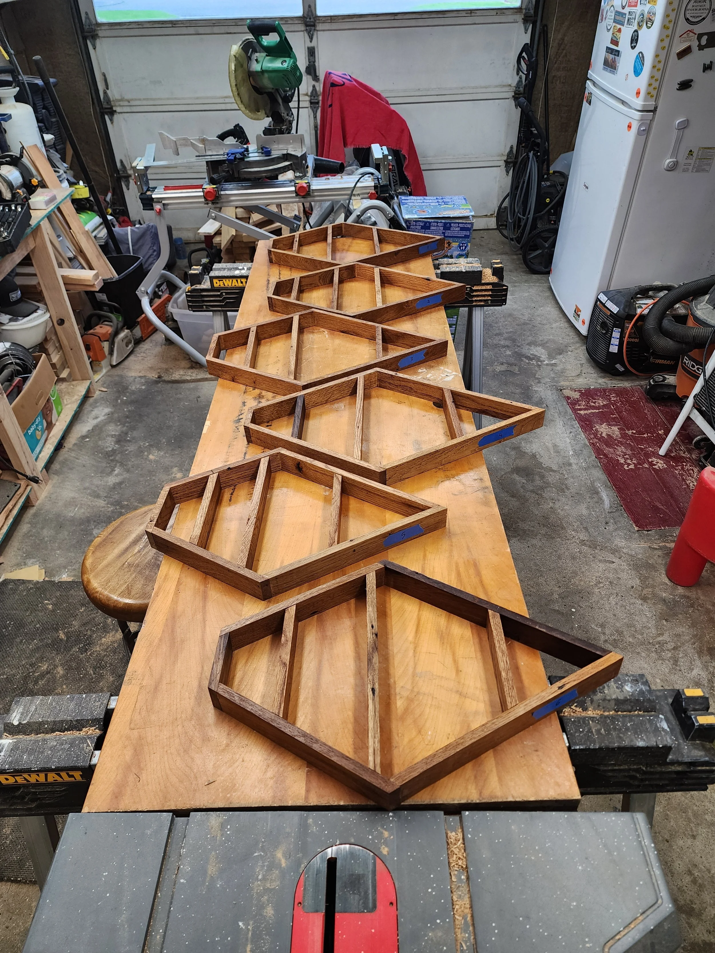 Six wooden diamond-shaped frames arranged in a row on a workbench in a woodworking shop.