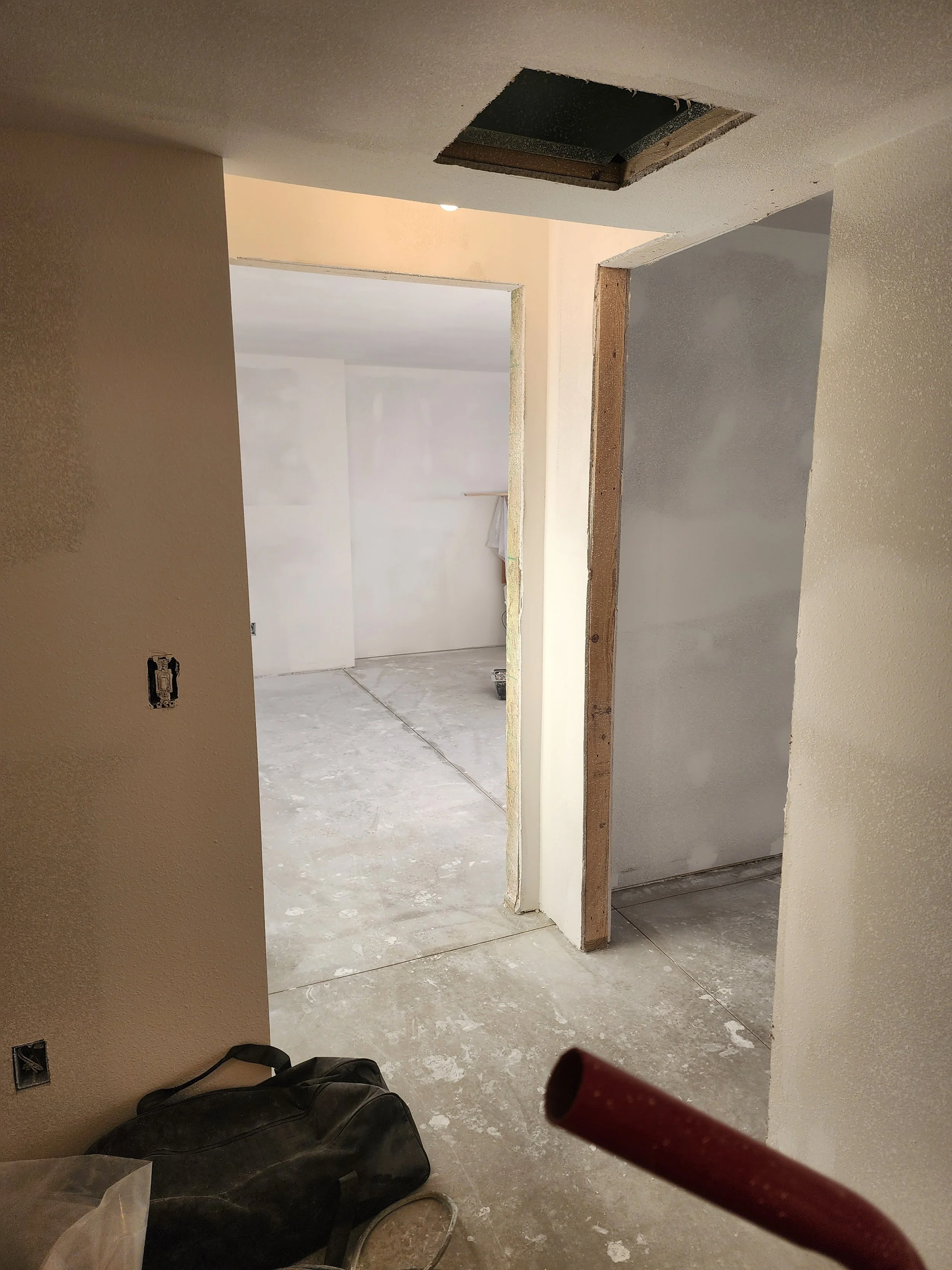 Interior of a house under construction, showing unfinished walls, a hole in the ceiling, and construction tools and materials on the floor.