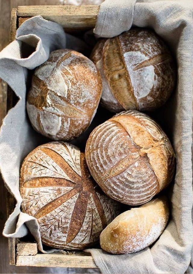A rustic wooden crate containing five loaves of bread, lined with beige linen cloth.