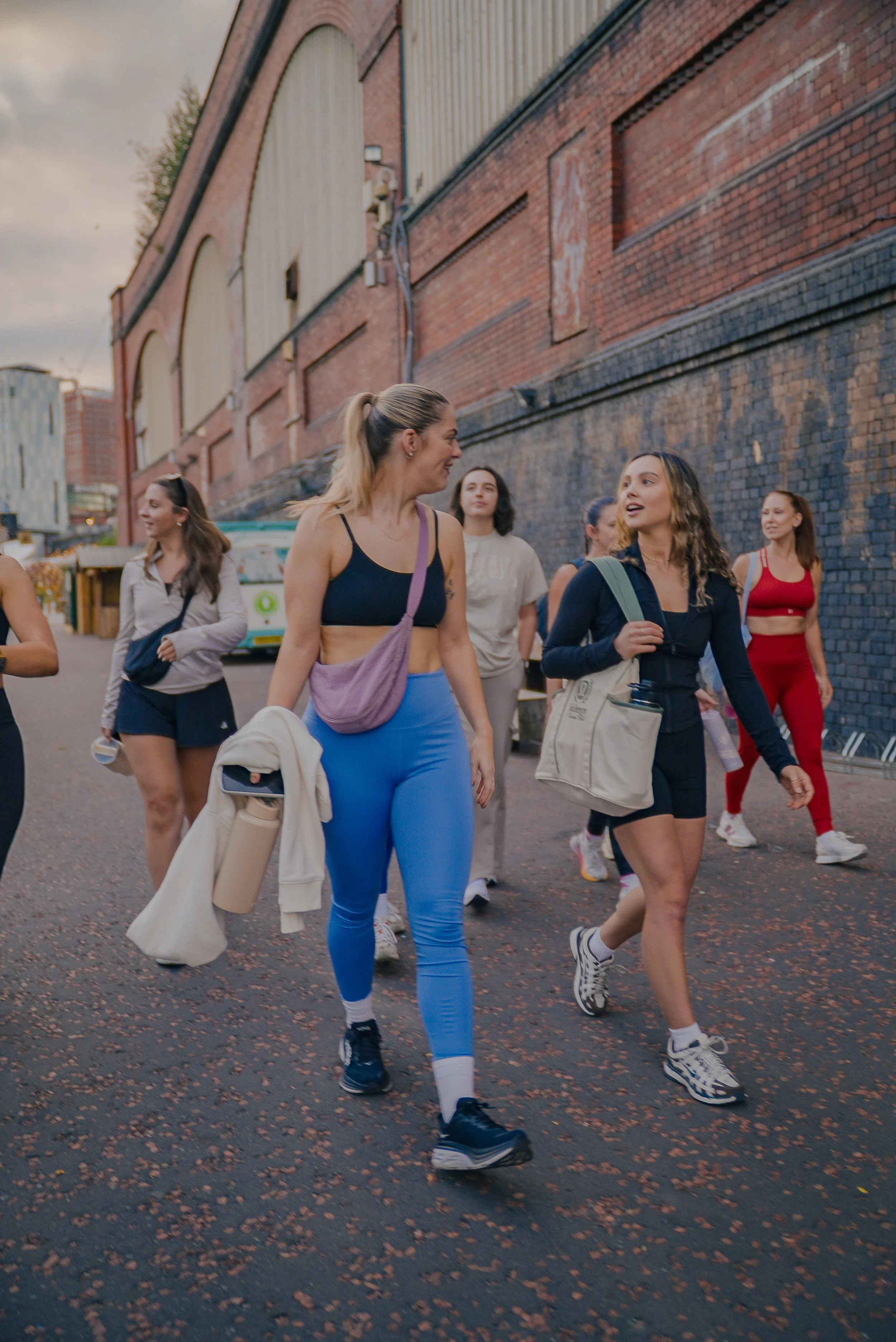 Group of women walking together in athletic wear outside near a brick building.