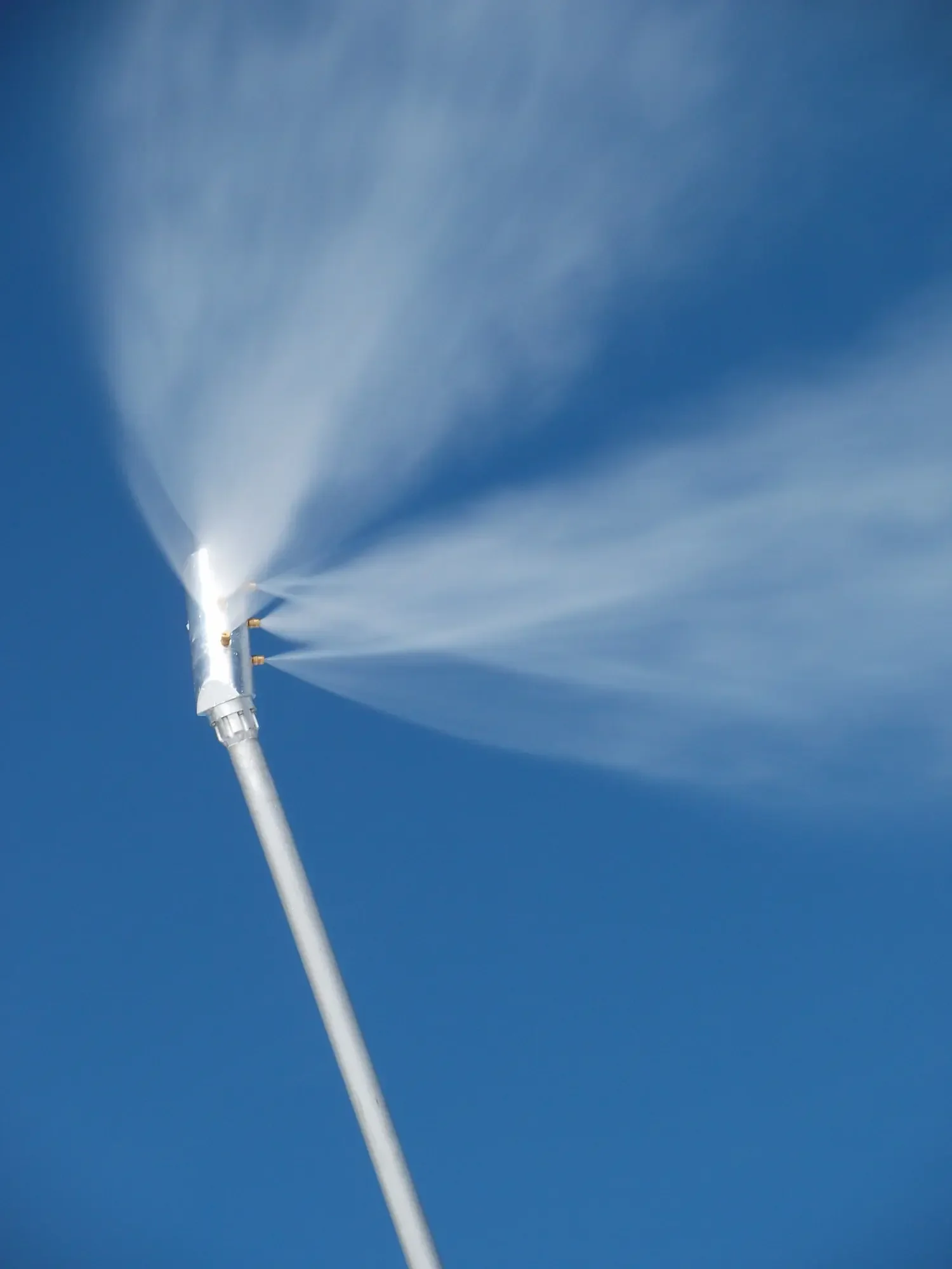 A high-pressure water hose spraying water against a clear blue sky.