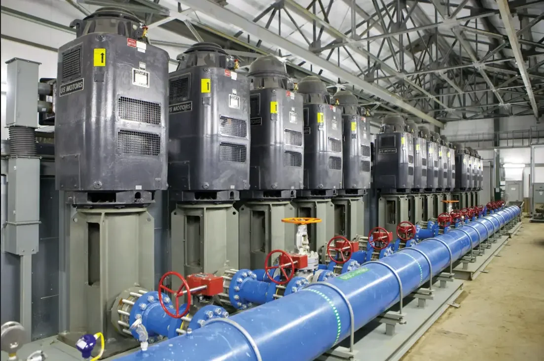 A worker inspecting blue industrial pipes connected to a mechanical system in an industrial setting.