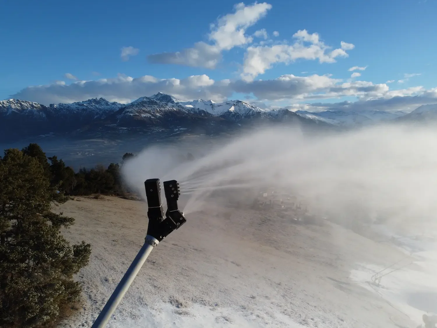 A robot arm spraying mist on a mountain landscape with snowy peaks, green trees, and blue skies.