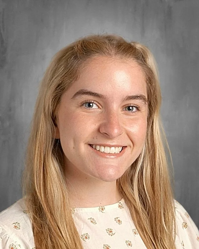 A young woman with long blonde hair smiling against a gray background.