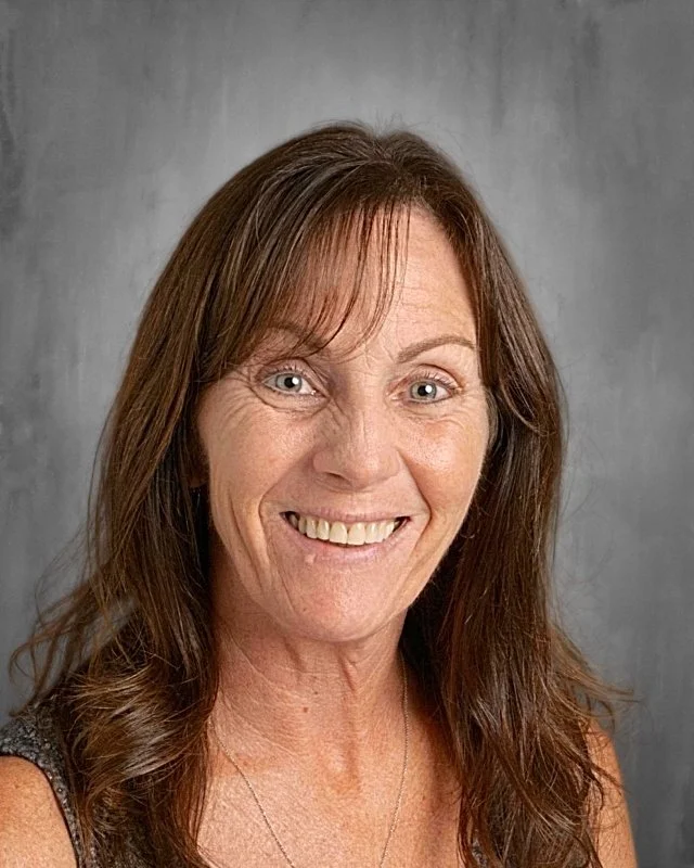 A smiling woman with shoulder-length brown hair and a light complexion posing against a gray background.