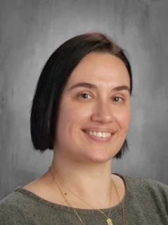 Portrait of a woman with dark hair in a bob style, wearing a striped shirt, smiling lightly, against a gray background.