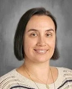 Portrait of a woman with dark hair in a bob style, wearing a striped shirt, smiling lightly, against a gray background.